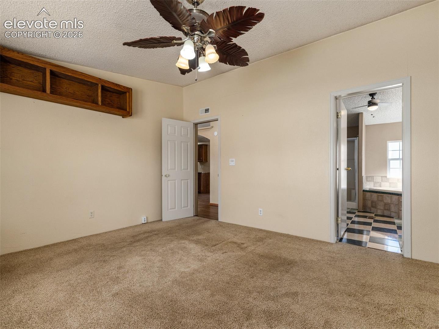 Room featuring wall-to-wall carpeting, a multi-blade ceiling fan with integrated lighting, built-in wooden shelving, and a six-panel interior door