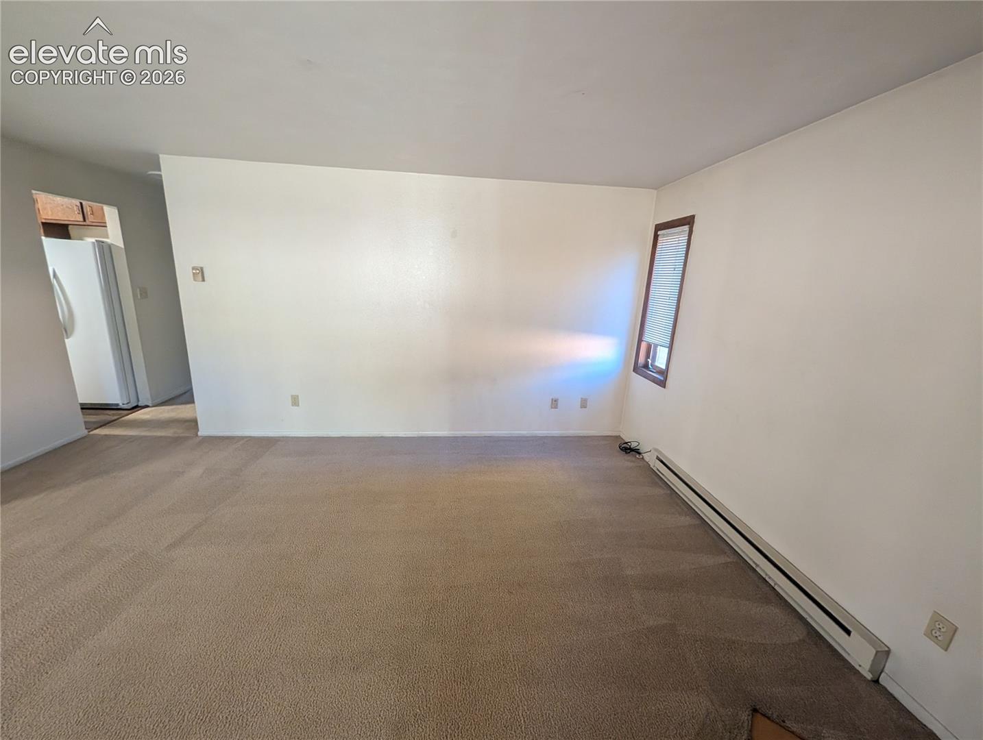 Carpeted living area with white walls and a window with wood trim