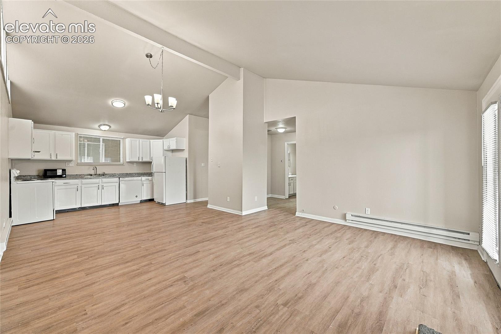 Open-concept interior featuring vaulted ceilings, wood-finish flooring, white cabinetry, and recessed lighting
