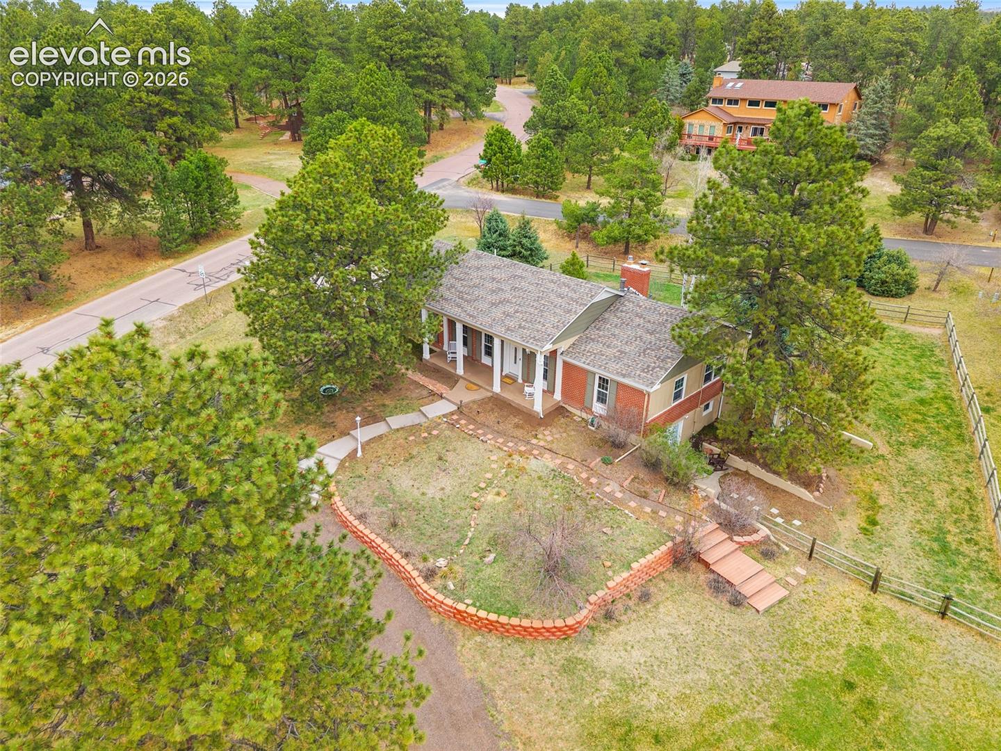 Single-story residence featuring a brick and siding exterior, covered front porch, tiered stone retaining walls, paved walkway, and a landscaped lot with mature coniferous trees