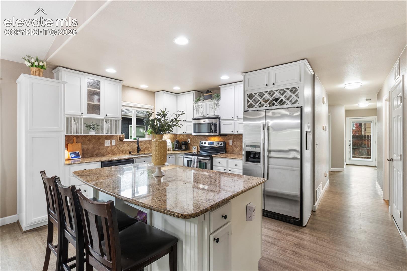 Kitchen featuring white cabinetry with glass-front uppers, stone-finish countertops, a center island, built-in wine storage, and wood-finish flooring