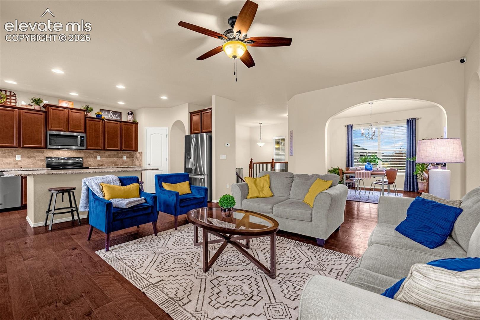 Open-concept living space featuring wood-finish flooring, dark-stained wood cabinetry, recessed lighting, a ceiling fan with integrated lighting, and an arched entryway