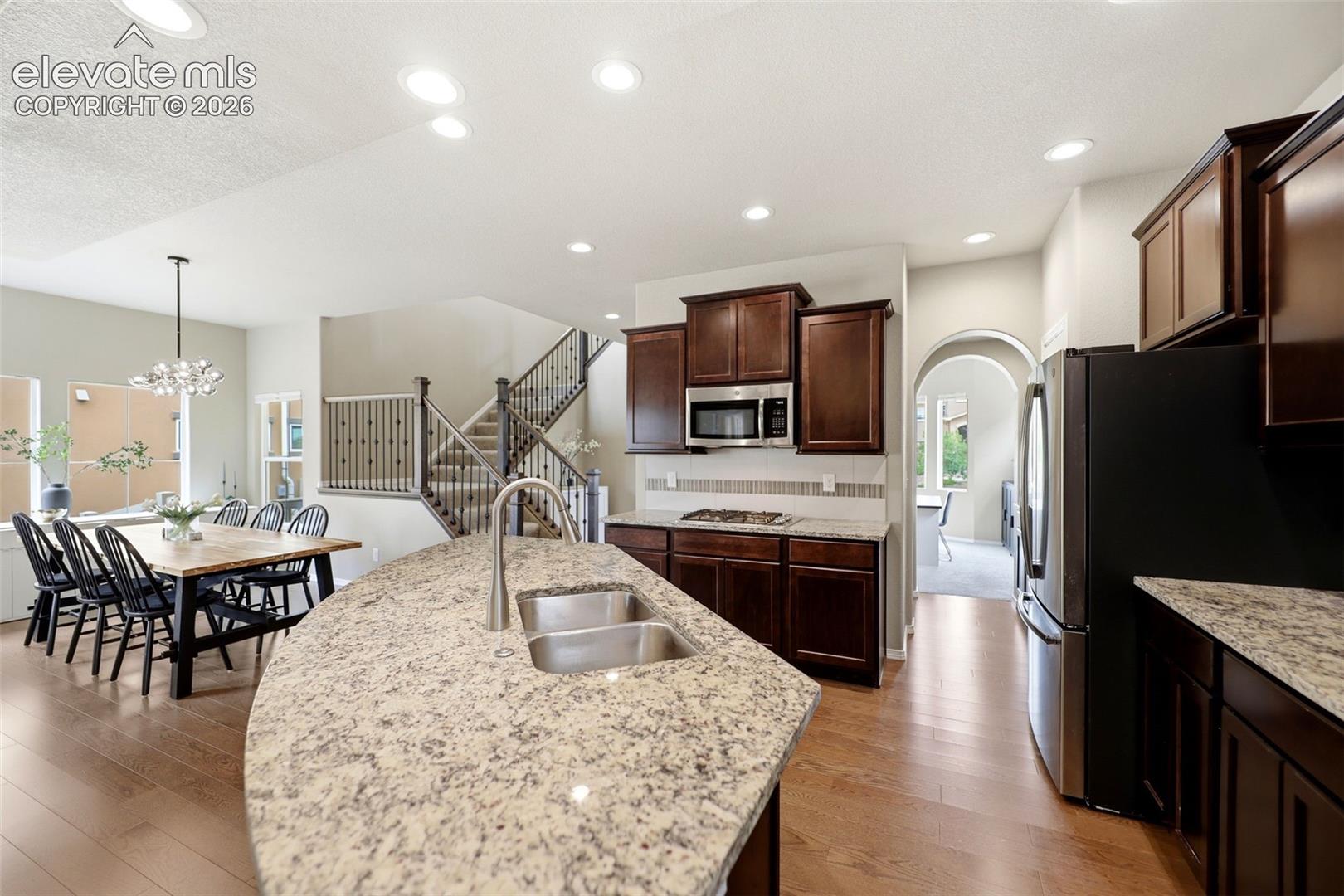 Spacious kitchen featuring an expansive island with a double sink, dark wood-finish cabinetry, built-in stainless steel microwave, and wood flooring