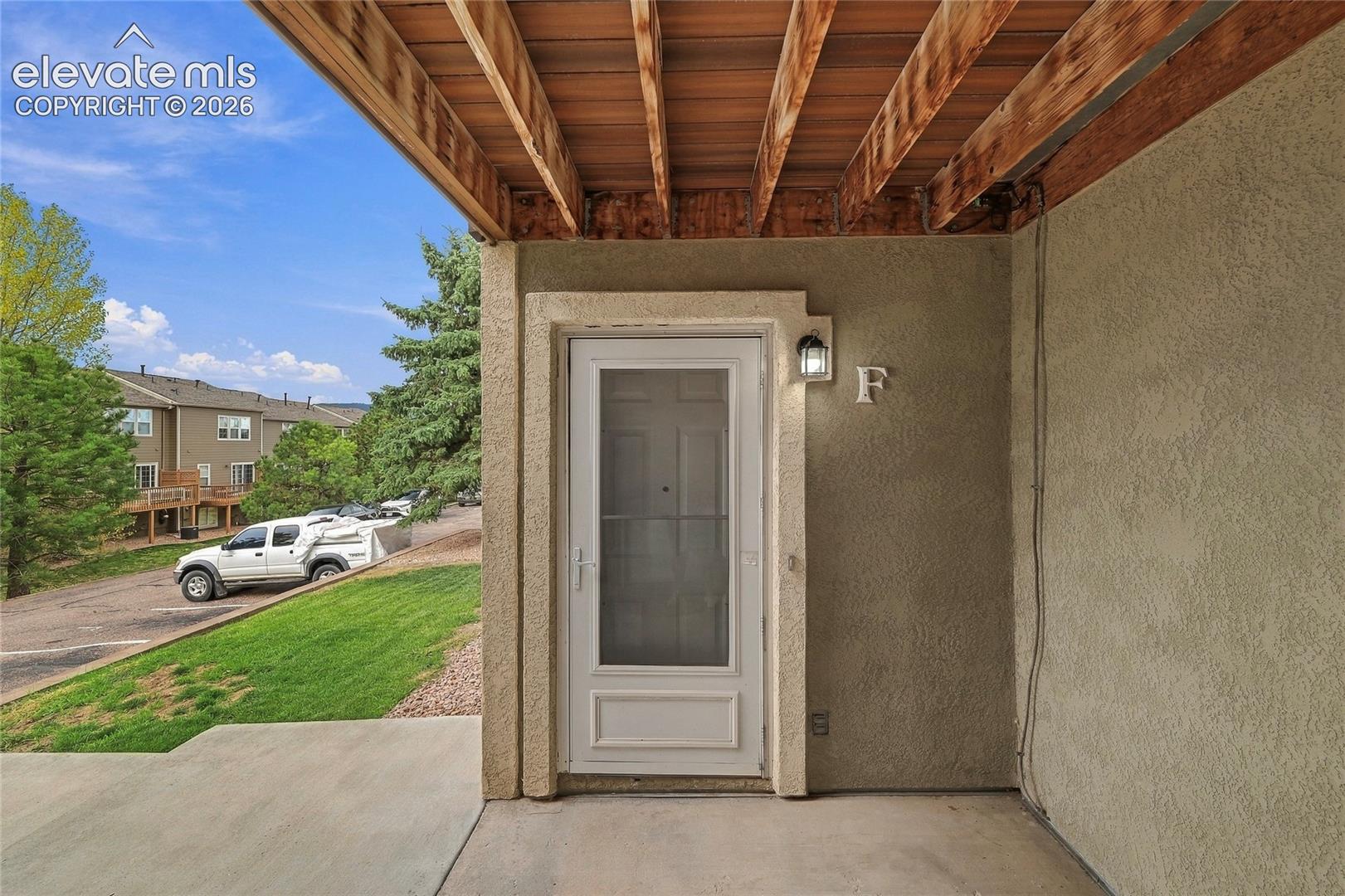 Covered entryway featuring exposed wood ceiling joists, a textured stucco exterior, and a single-light storm door with integrated hardware