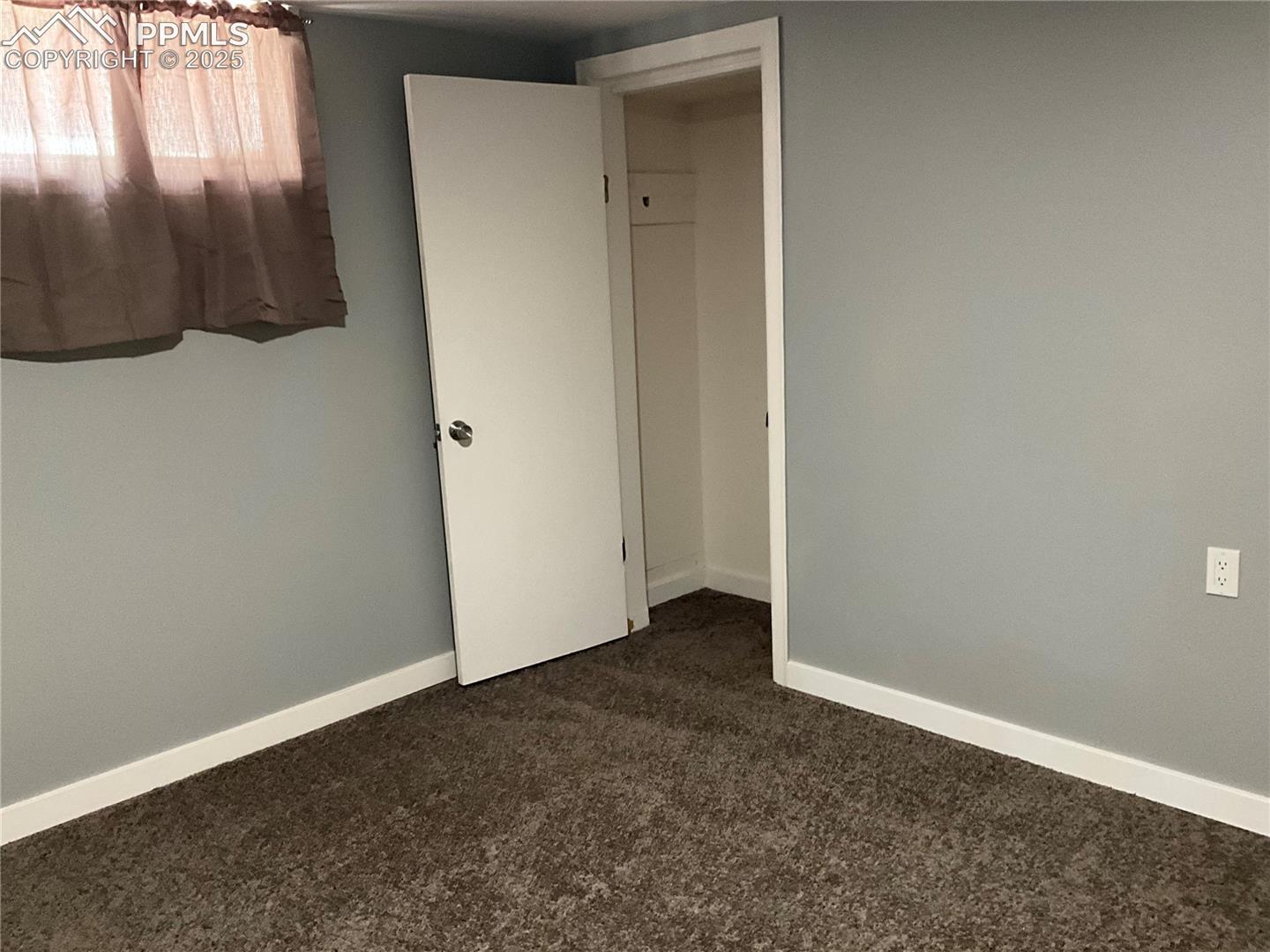 Unfurnished bedroom with dark colored carpet and baseboards