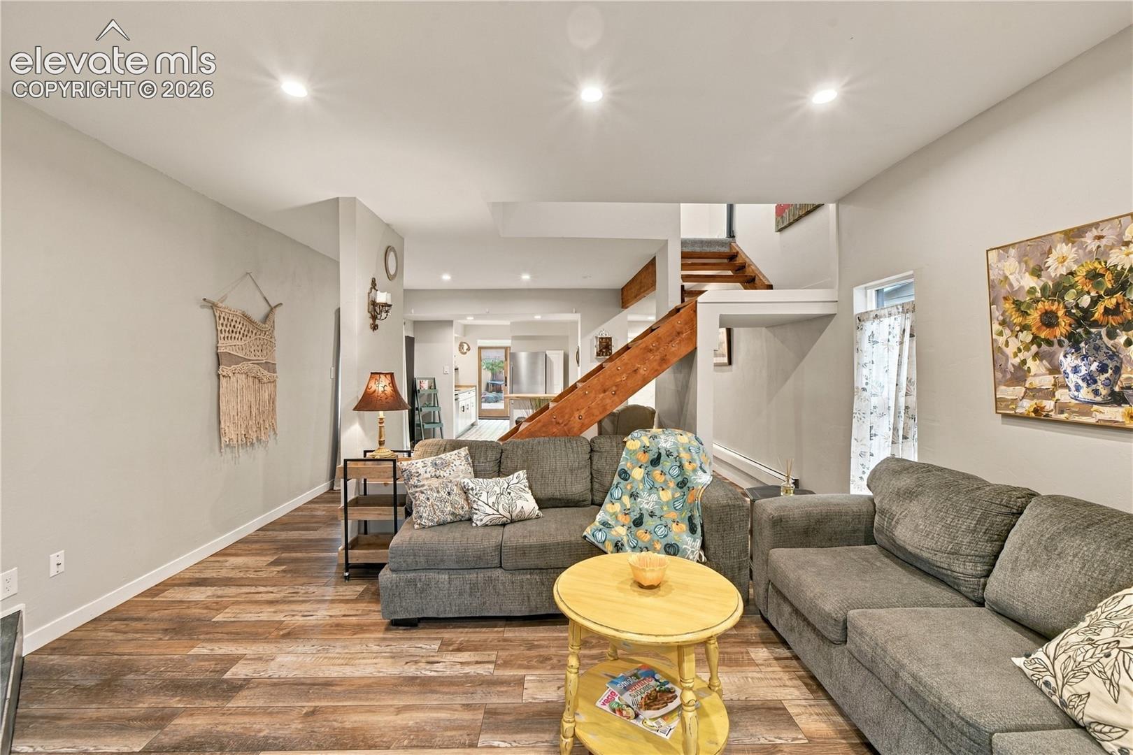 Open-concept living space featuring recessed lighting, wood-finish flooring, and an architectural staircase with stained wood treads
