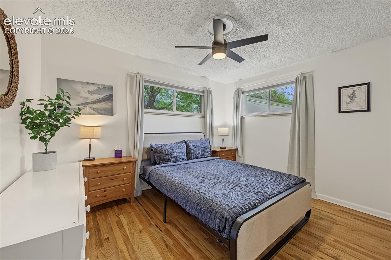 Room featuring wood-finish flooring, dual horizontal windows, and a ceiling-mounted light fixture with fan blades