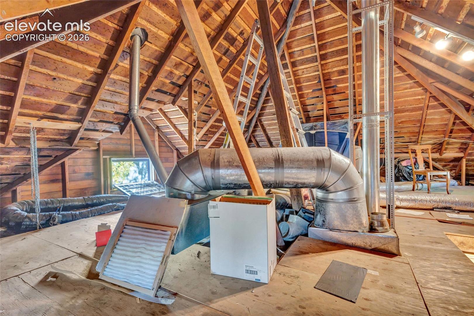 Attic space featuring exposed timber framing, wood plank subflooring, metal ductwork, and an installed ventilation system