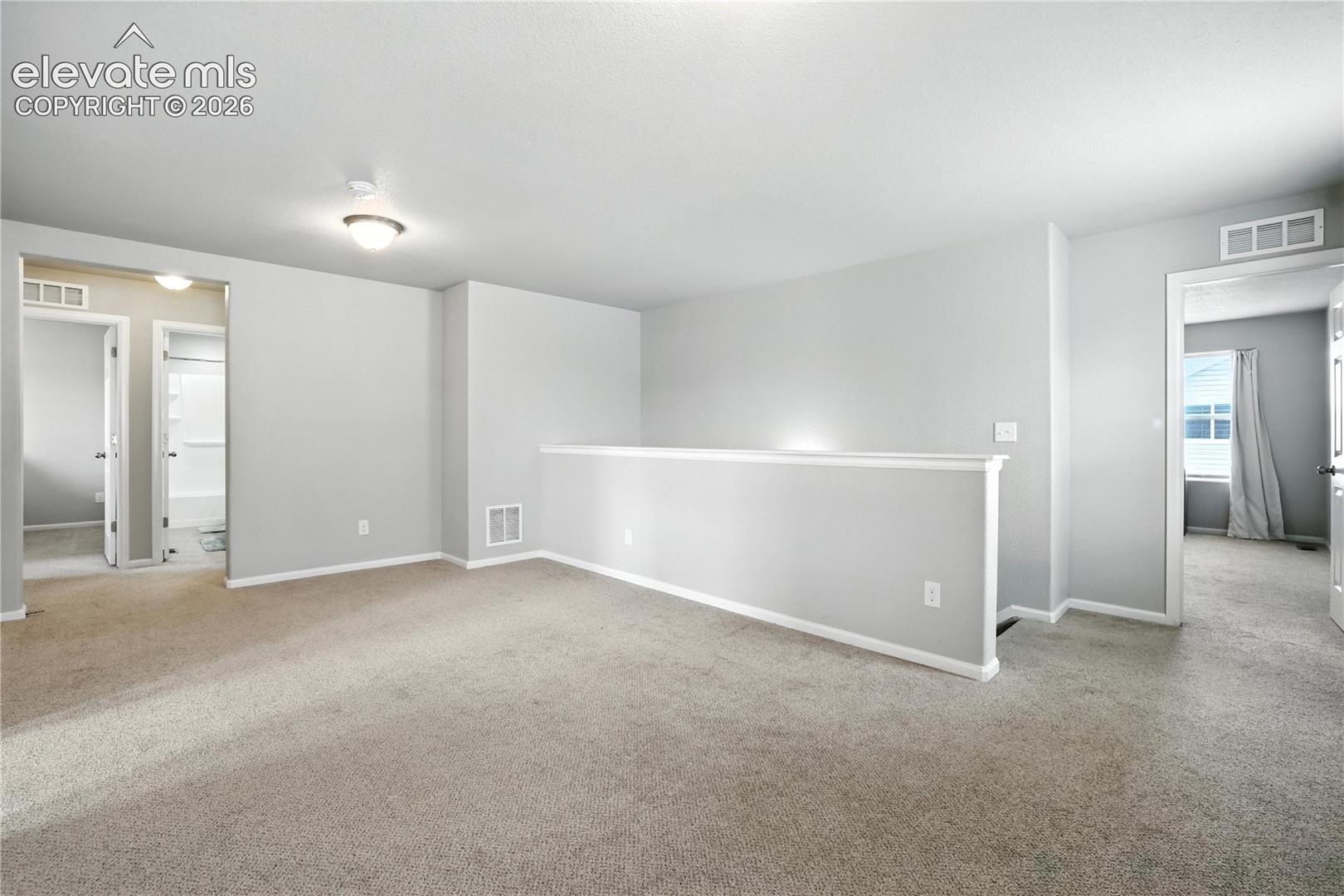 Carpeted floor, neutral wall paint, overhead lighting, white trim, and a partial balustrade