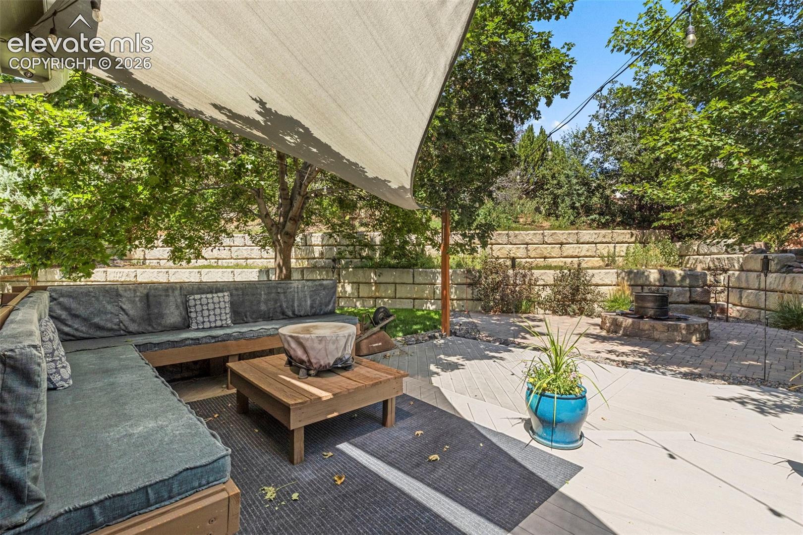 Private outdoor living space with a shade sail, built-in bench seating, wood-finish decking, and a paver patio with a fire pit