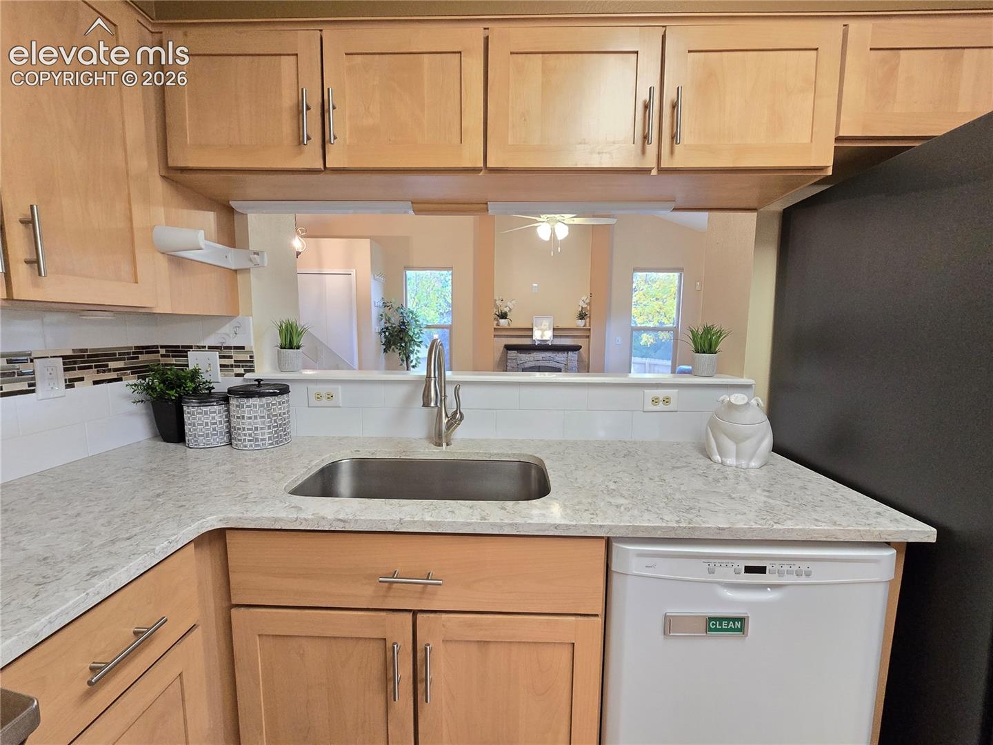 Kitchen featuring light wood-finish cabinetry, stone-finish countertops, stainless steel undermount sink with a pull-down faucet, and decorative tile backsplash