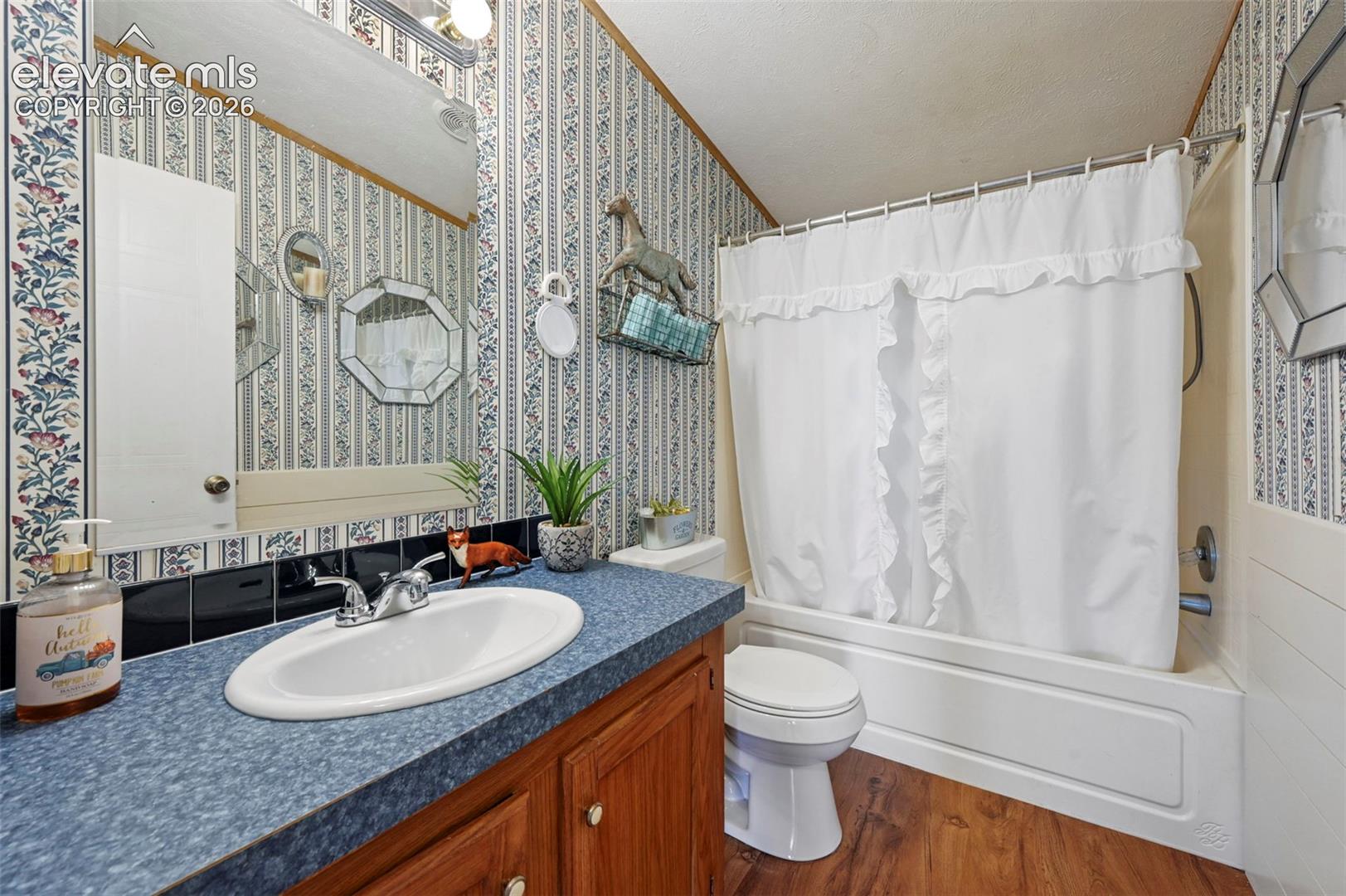 Bathroom featuring a wood-finish vanity with a blue laminate countertop, integrated sink, wall-mounted mirror, and a tub-shower combination with a white surround