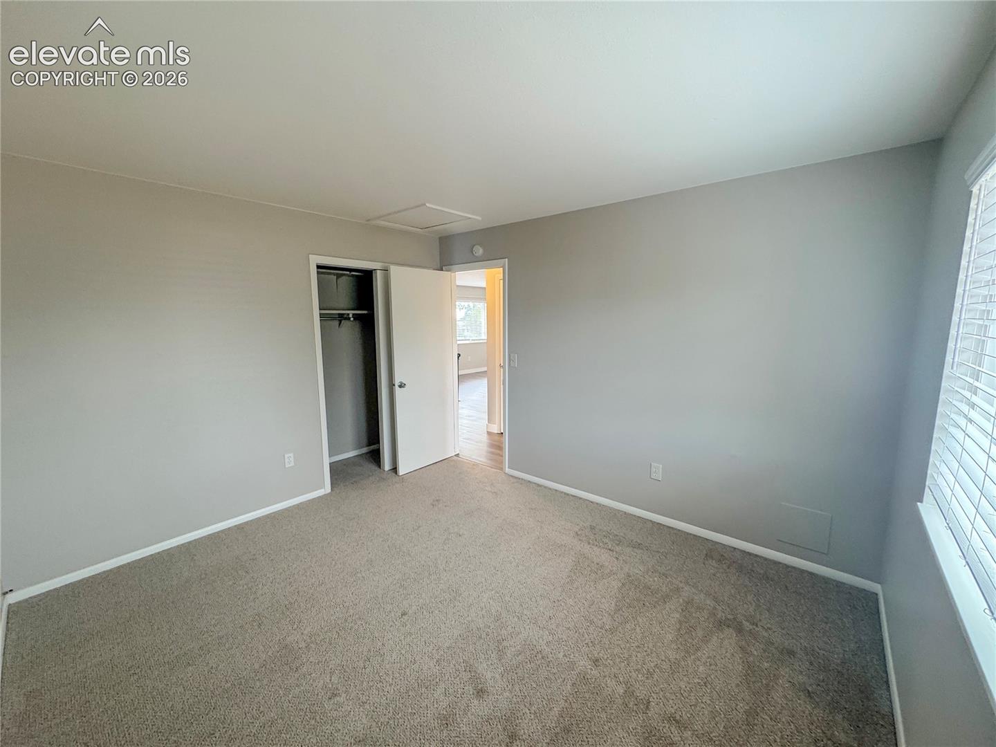 Neutral-toned interior room featuring wall-to-wall carpeting, an integrated closet, and a multi-pane window with blinds