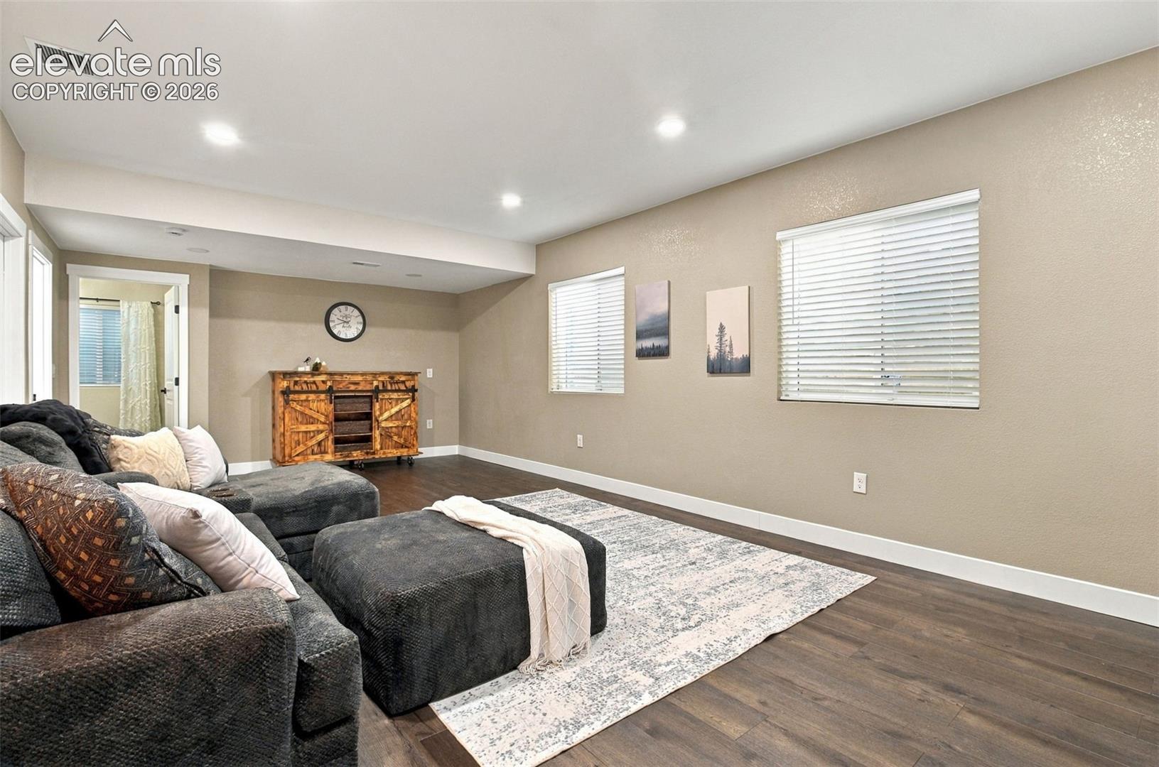Neutral-toned interior space featuring wood-finish flooring, recessed lighting, and dual windows with horizontal blinds