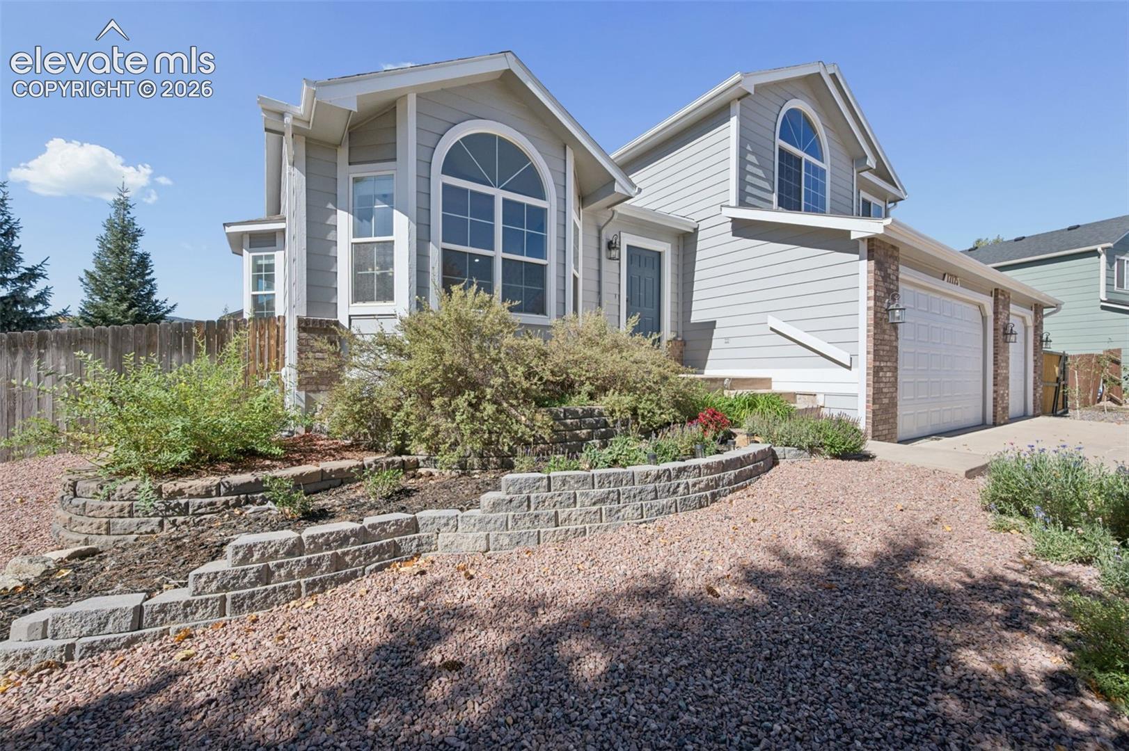 Multi-level exterior featuring light gray horizontal siding, arched windows, decorative brick accents, and a tiered stone block retaining wall