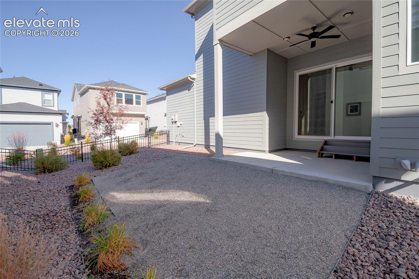 Covered patio with a ceiling fan, concrete flooring, sliding glass door, and gravel-based backyard featuring a metal perimeter fence