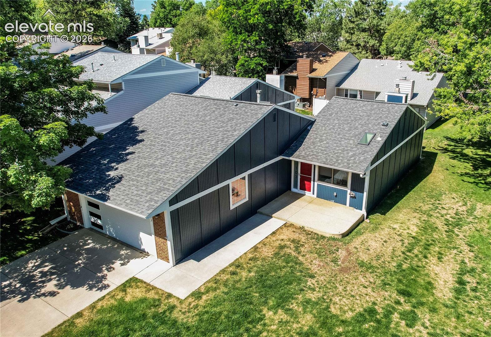 Split-level exterior featuring vertical siding, a composition shingle roof, a concrete driveway, a front concrete patio, and a roof-mounted skylight