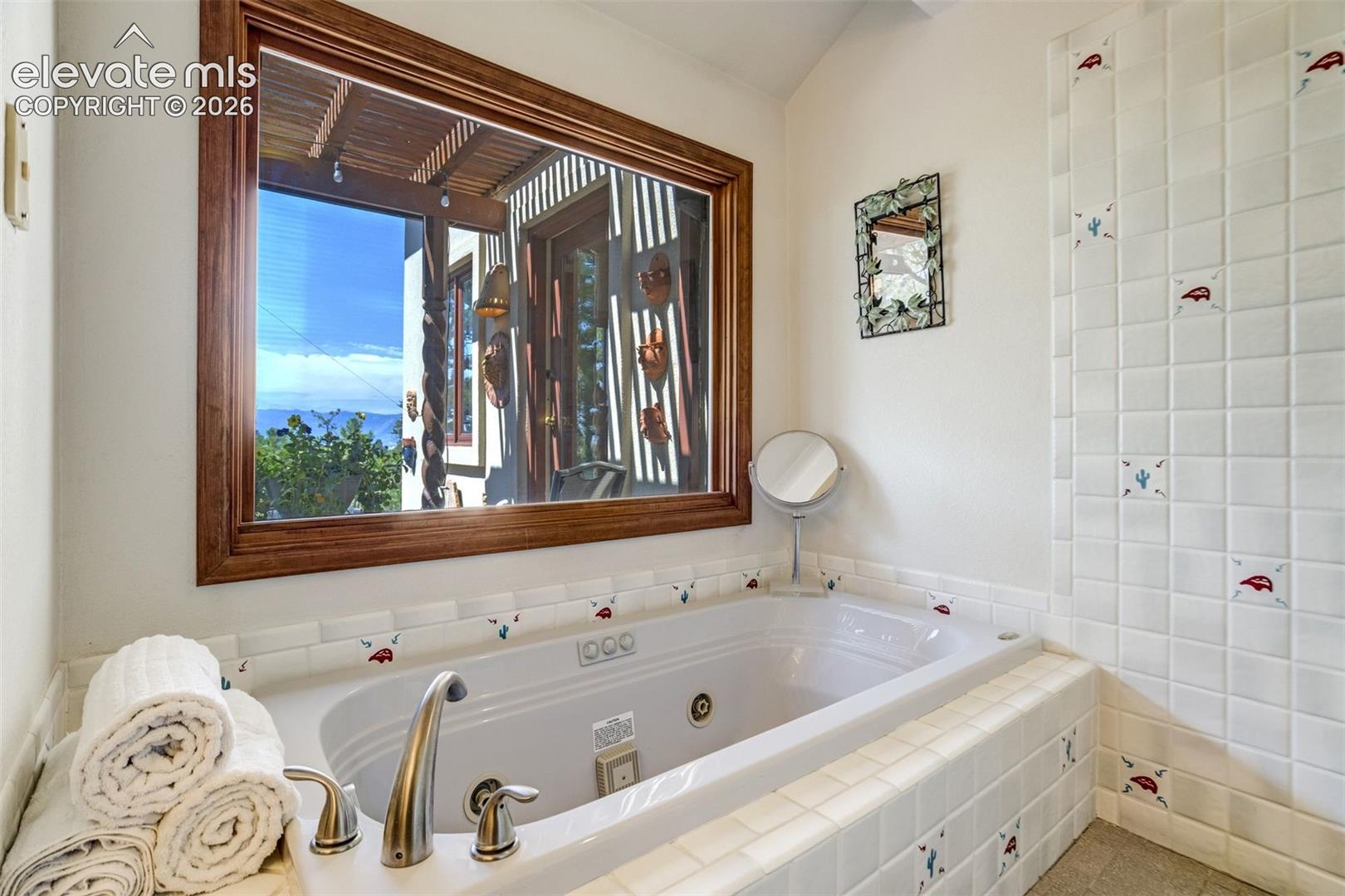 Jetted tub with mountain views framed in the window and walk-in shower to it's right