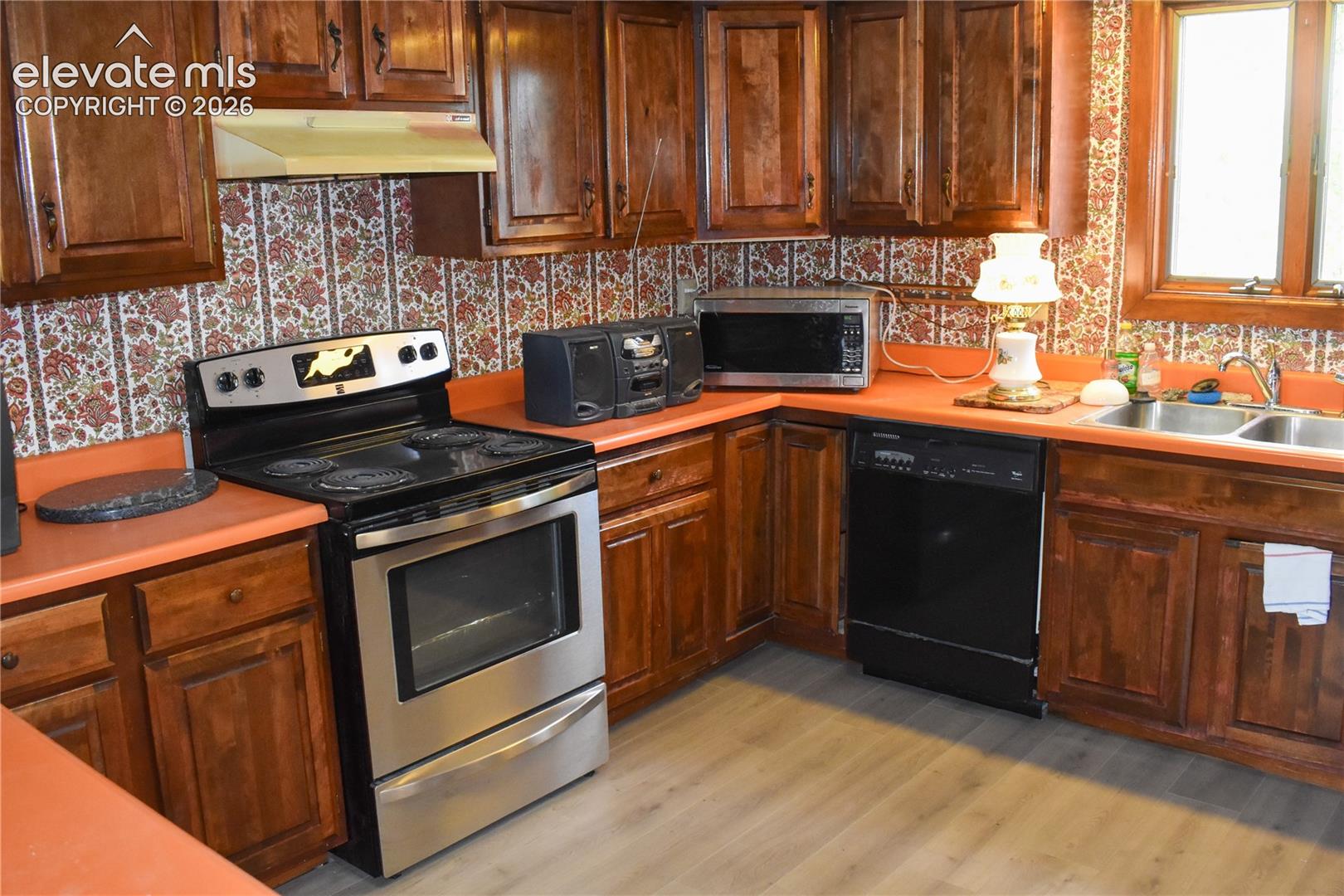 Wood-finish cabinetry paired with a stainless steel range, a dual-basin sink, and a built-in dishwasher