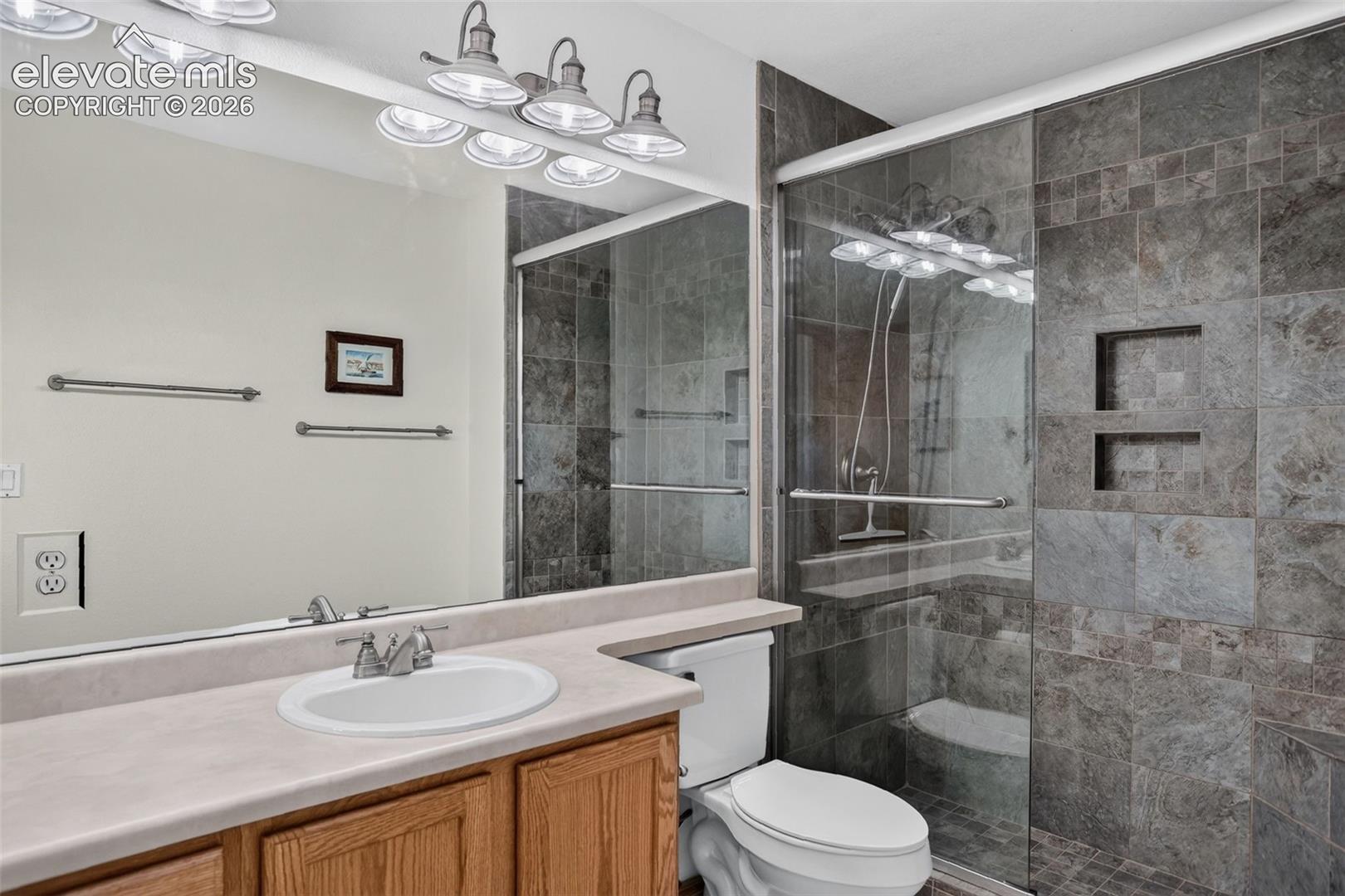 Full bathroom featuring a walk-in shower with glass enclosure, integrated shelving, and large format wall tiling