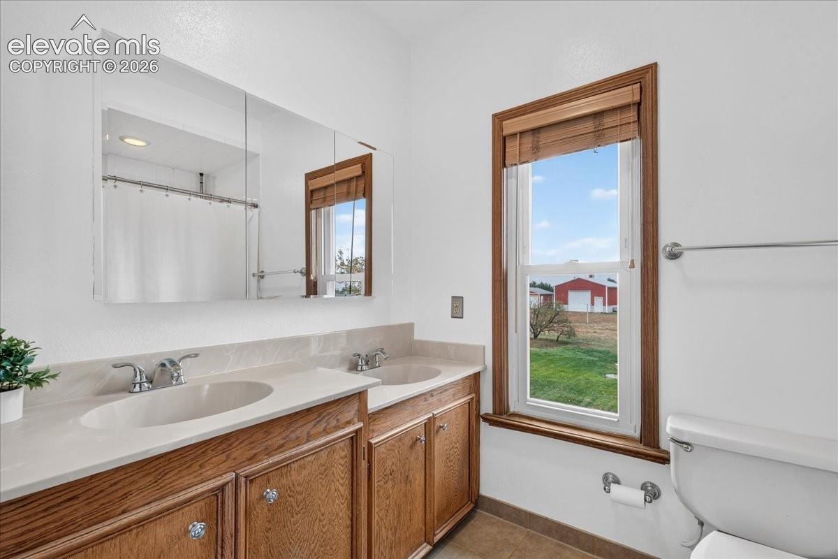 Double vanity with wood-finish cabinetry, solid-surface countertop, dual integrated sinks, and large tri-fold medicine cabinet