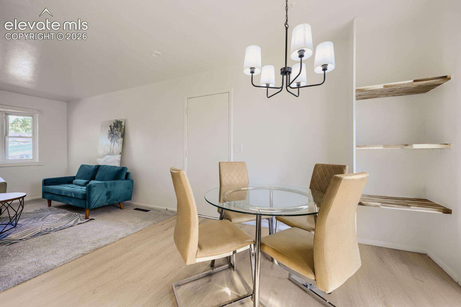 Open-concept living space with wood-finish flooring, a contemporary five-light chandelier, and built-in shelving