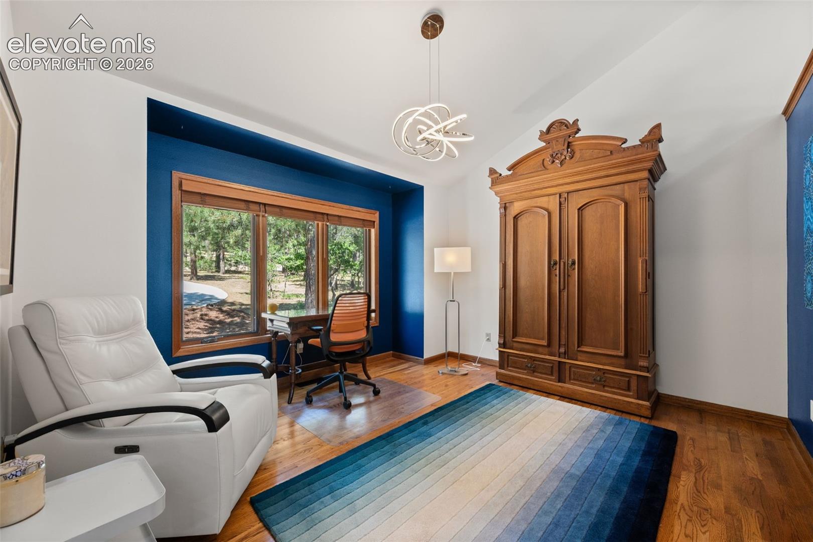 Spacious room featuring wood-finish flooring, a large window with wood trim, and a contemporary ceiling light fixture