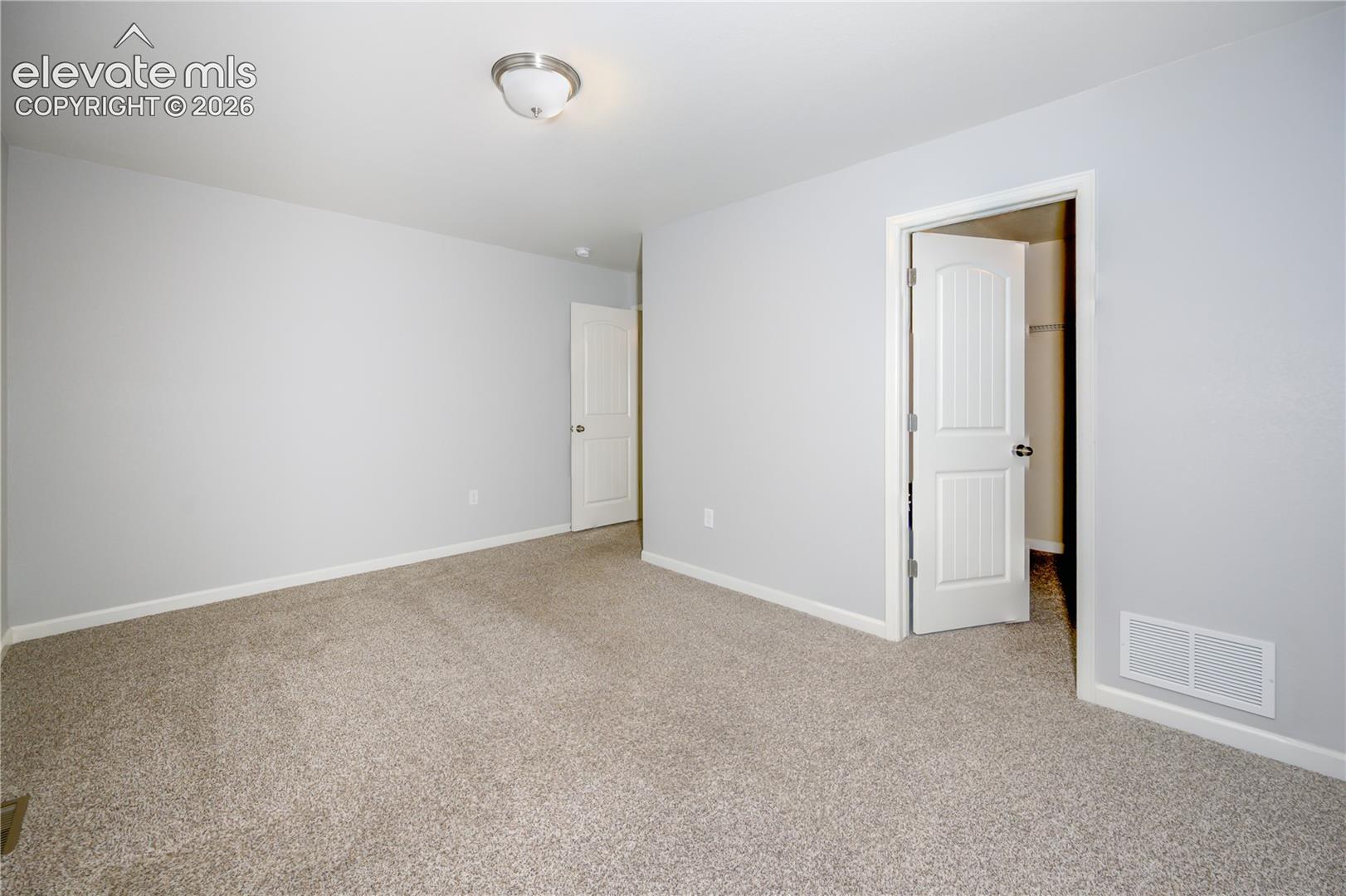 Neutral-toned interior space featuring wall-to-wall carpeting, flush-mount ceiling lighting, and two multi-panel interior doors