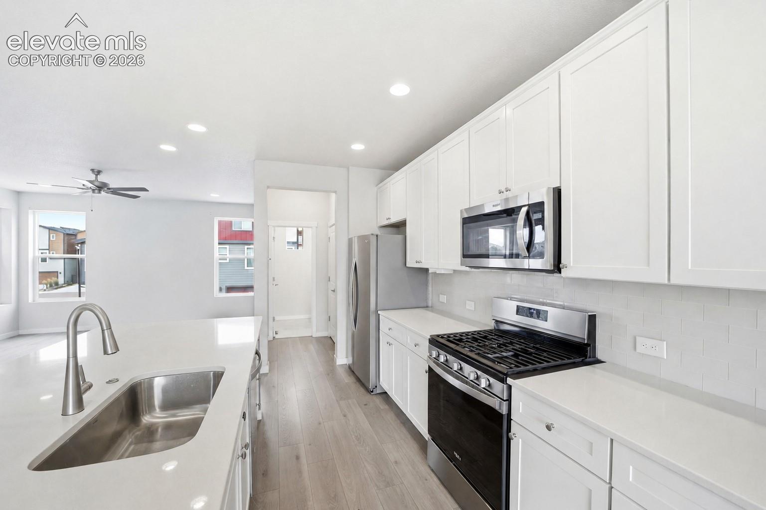 Kitchen featuring white cabinetry, stainless steel appliances, a double basin sink, and wood-finish flooring