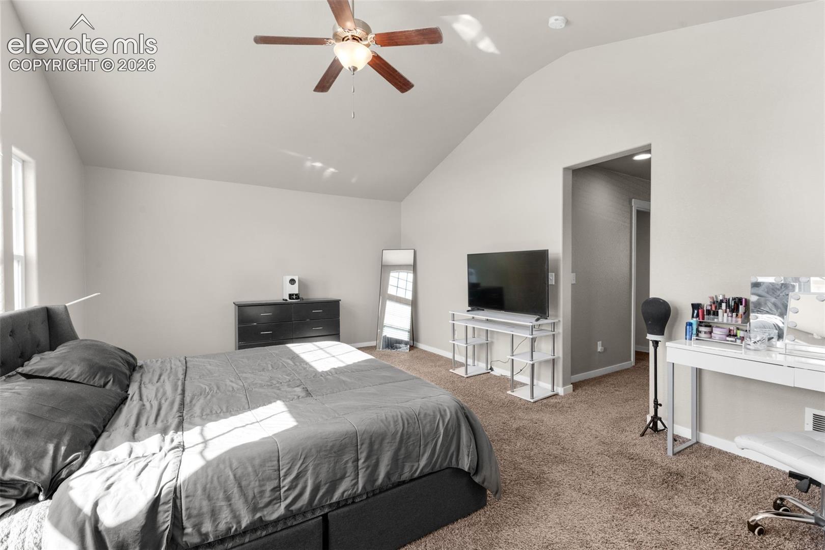 Vaulted ceilings, neutral wall tones, carpeted flooring, and a ceiling fan with integrated lighting