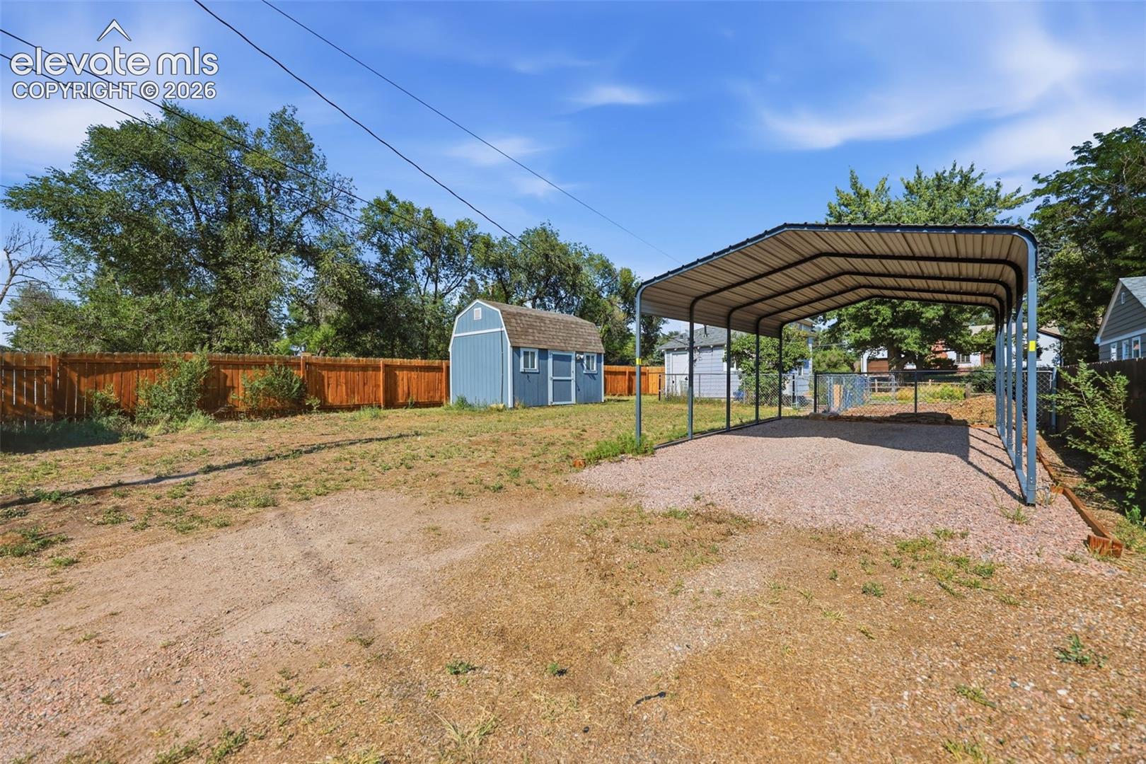 Spacious backyard featuring a utility shed with a shingle roof and two windows, a metal carport, and wood fencing.
