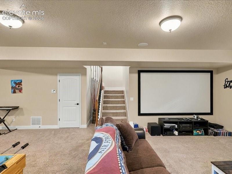 Built-in projection screen, recessed ceiling lighting, carpeted flooring, paneled interior door, and a carpeted staircase with wood handrail