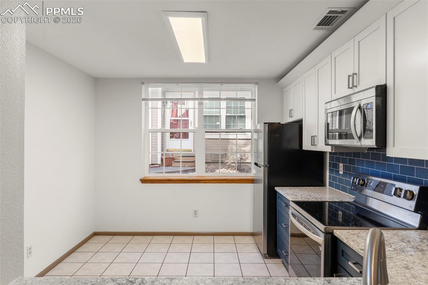 Two tone kitchen featuring stainless steel appliances, light stone counters, backsplash, and dual tone cabinets