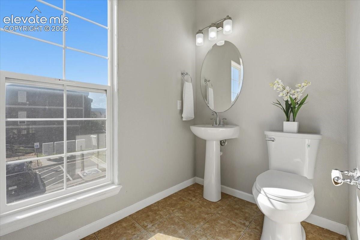 Main level powder room. Pedestal sink, Bright window, flush toilet, and wall-mounted vanity lighting