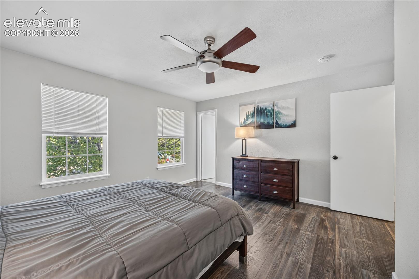 Wood-finish flooring, multi-pane windows with horizontal blinds, and a central ceiling fan with integrated lighting