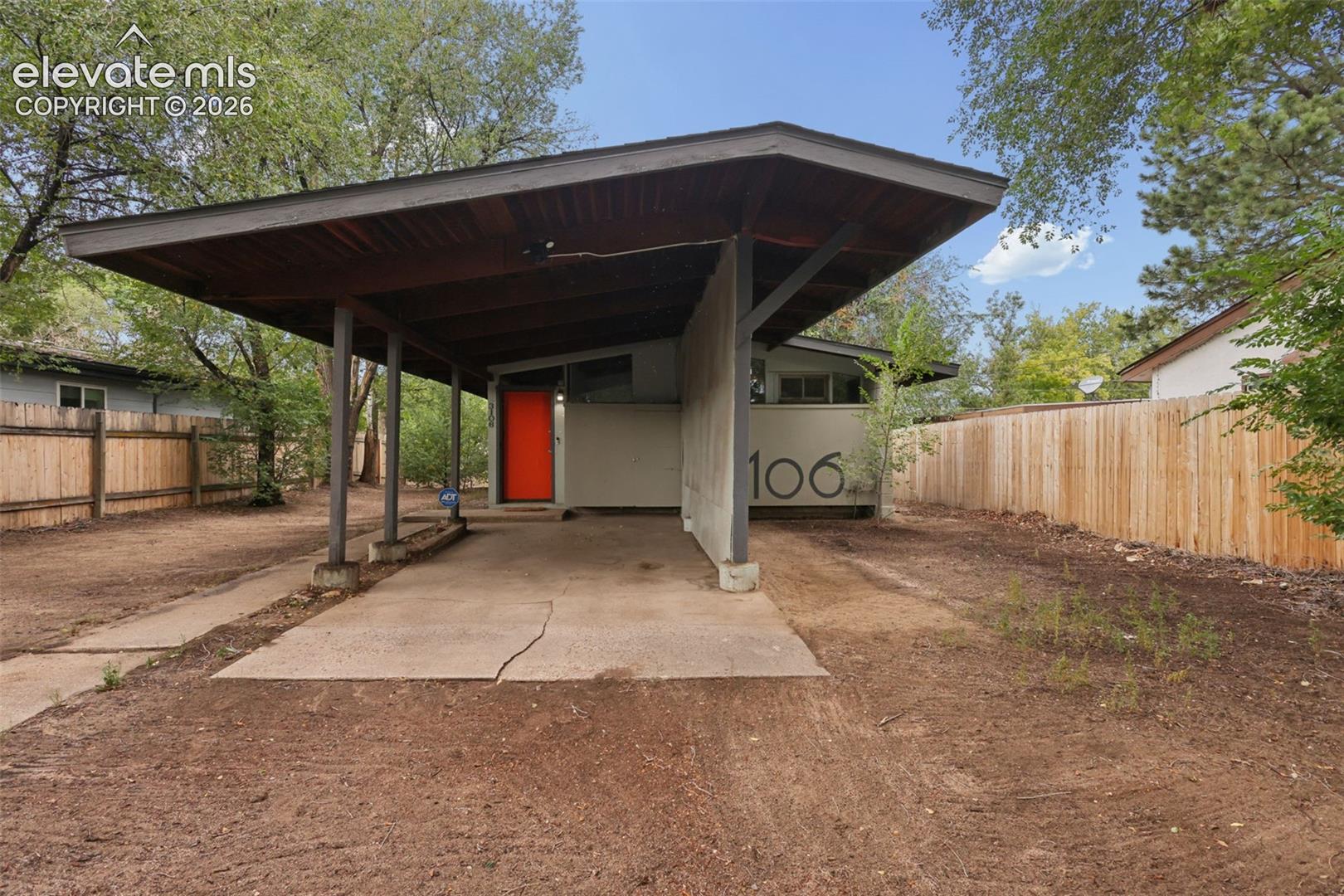 Mid-century modern residence featuring a prominent carport with a wood-finish ceiling, an orange entry door, and a horizontal house number display