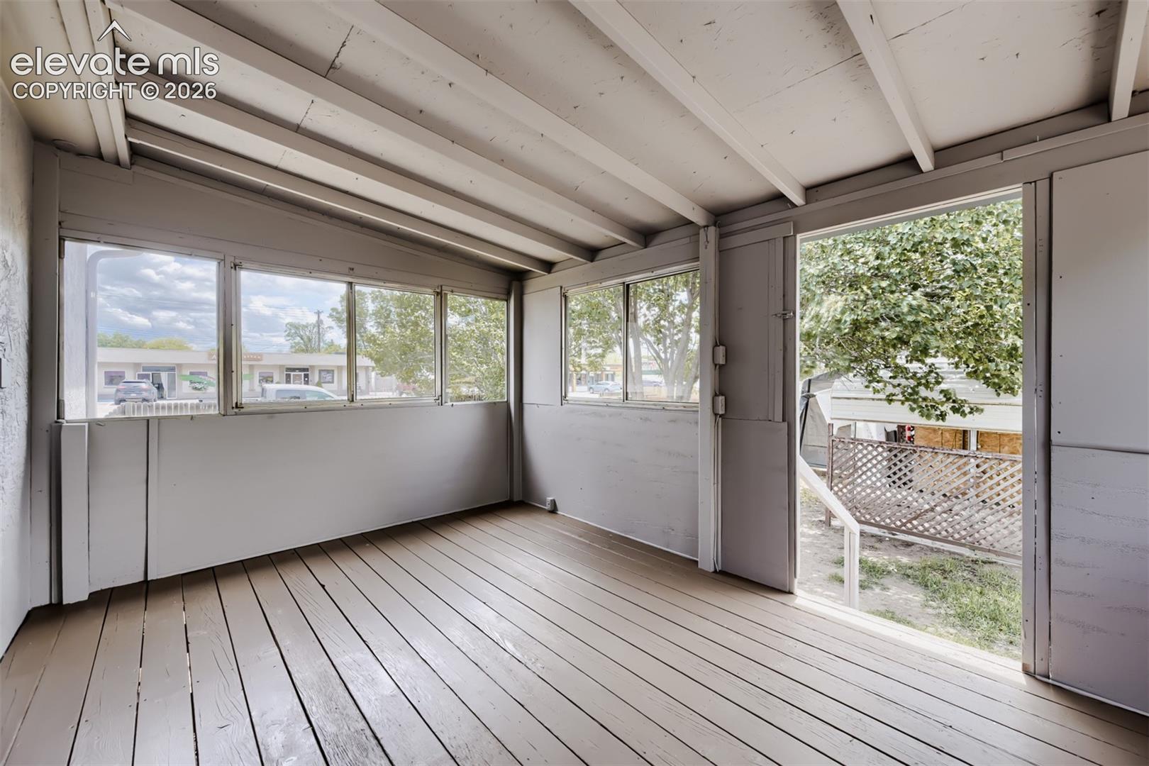 Covered outdoor patio with exposed beam ceiling, wood-finish flooring, and multiple windows