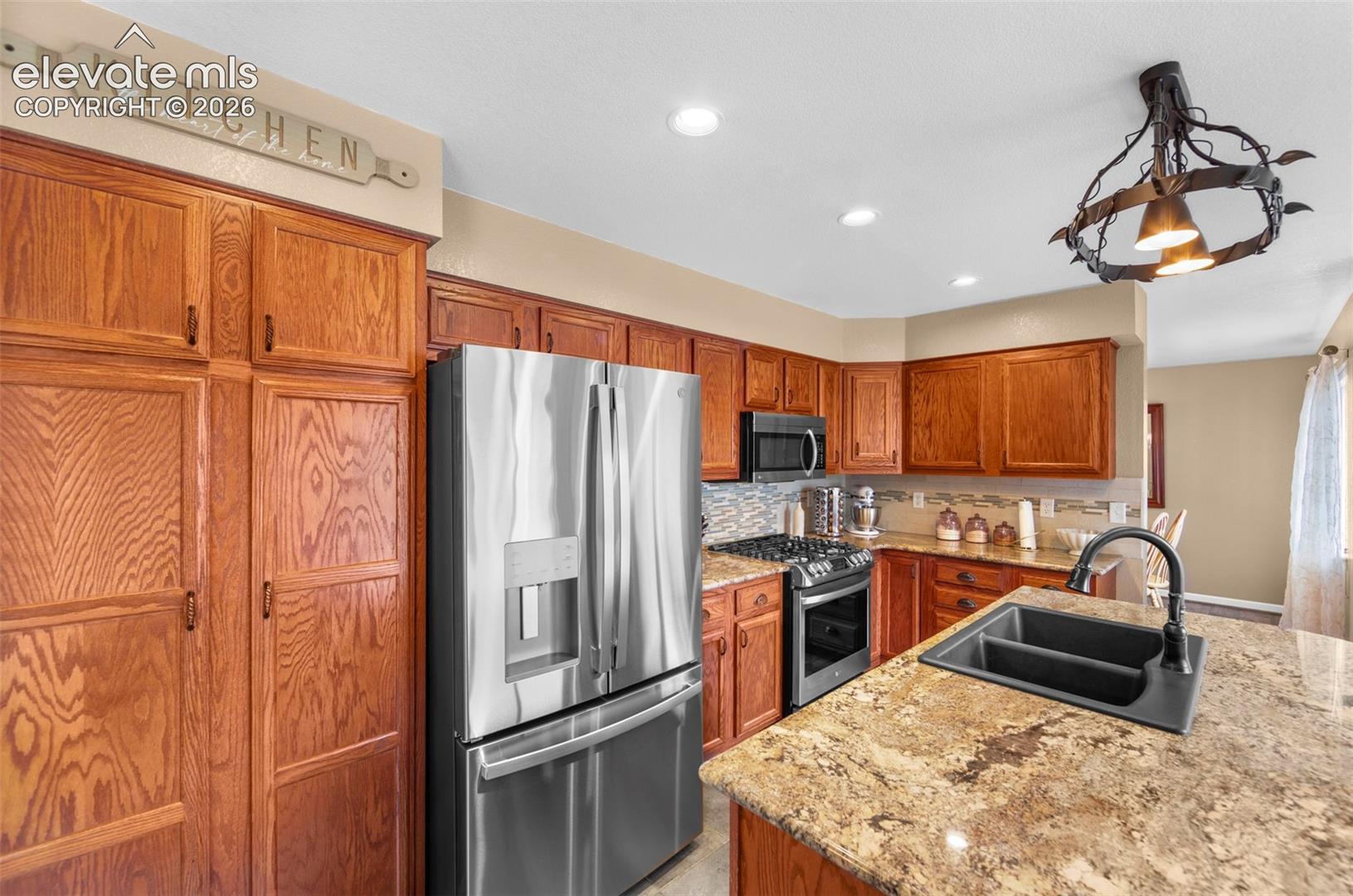 Kitchen featuring wood cabinetry, stainless steel appliances, granite countertops, a tile backsplash, and an undermount sink with a matte black faucet