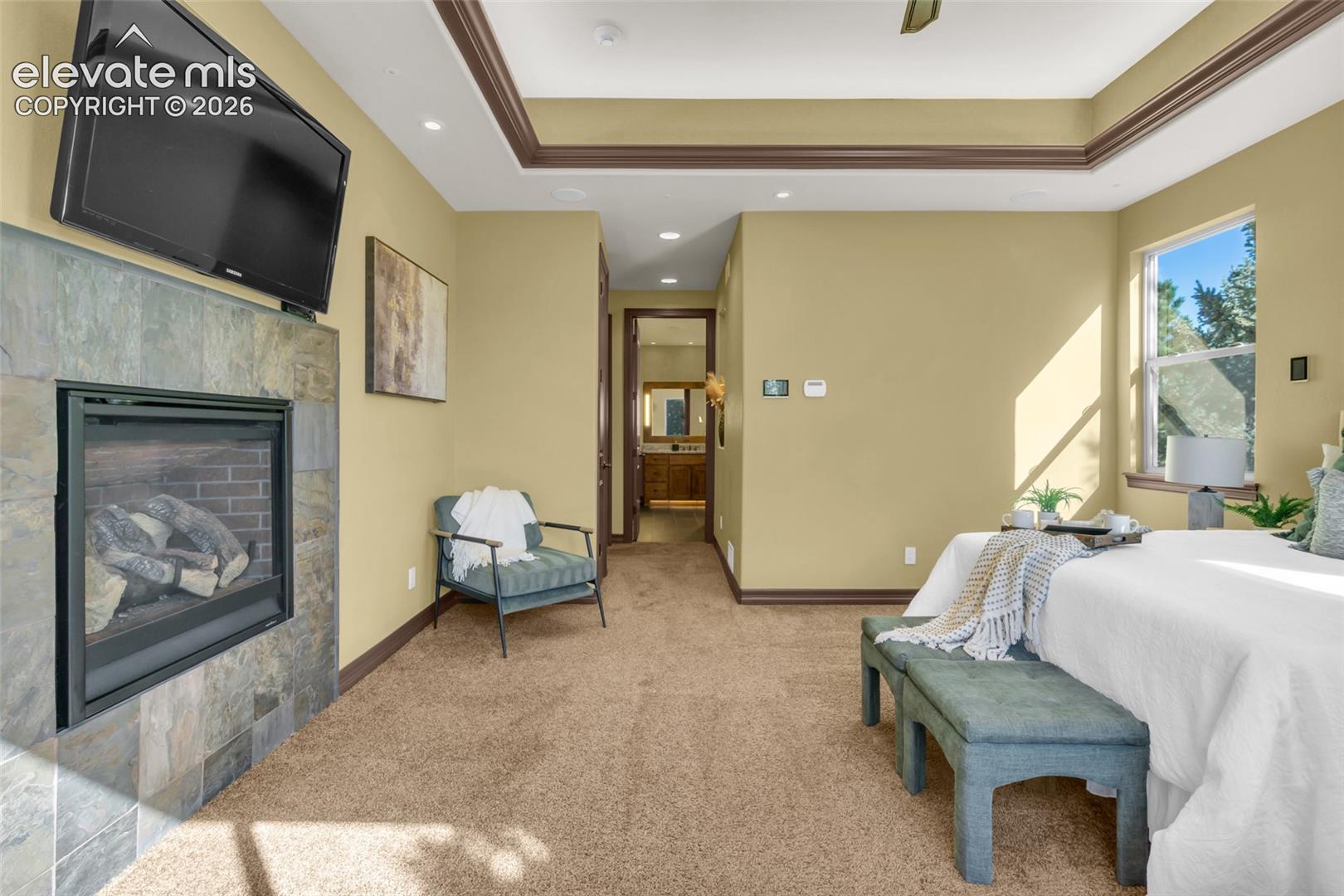 Tray ceiling with crown molding, stone-surround fireplace, recessed lighting, and wall-to-wall carpeting