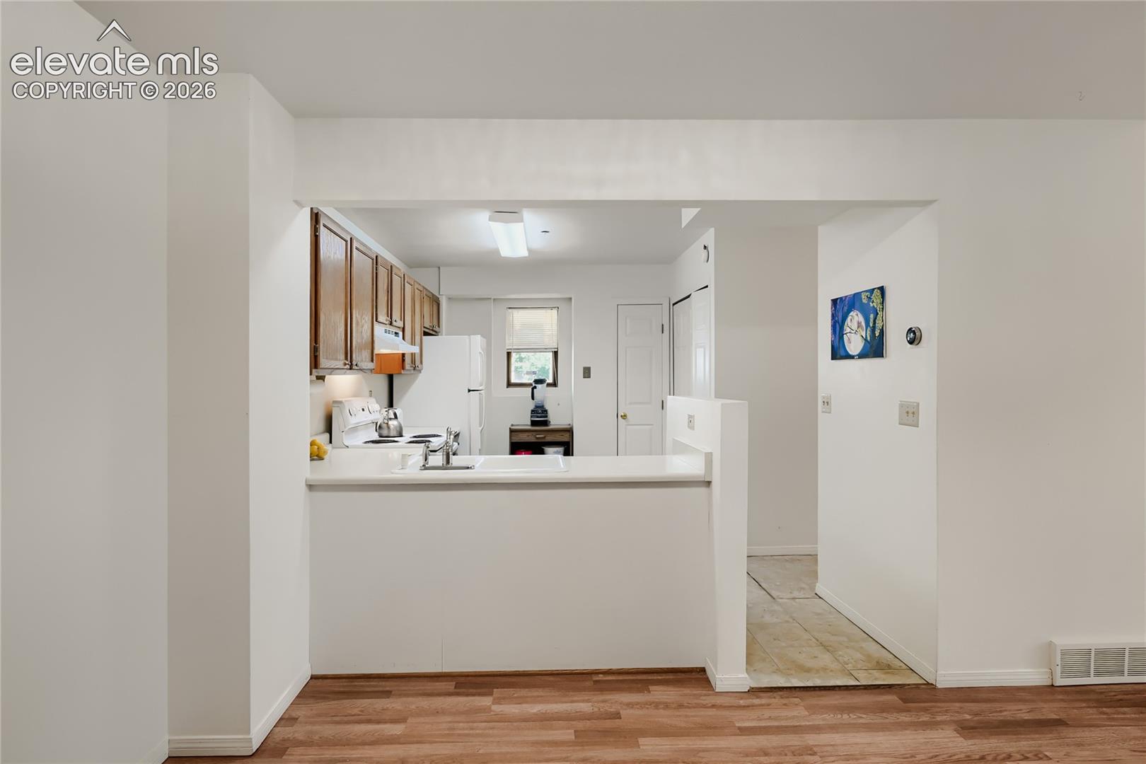 Kitchen with wood-finish cabinetry, white countertops, a stainless steel sink, and white appliances