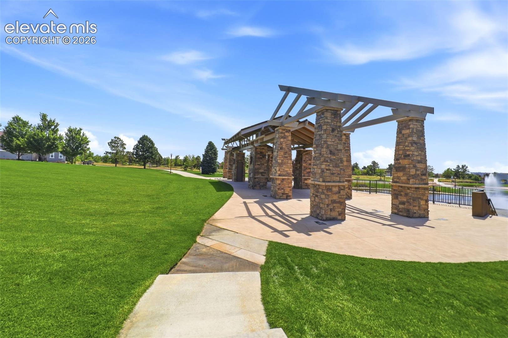 Expansive green space featuring a stone and wood beam pergola, a paved patio, and a water feature