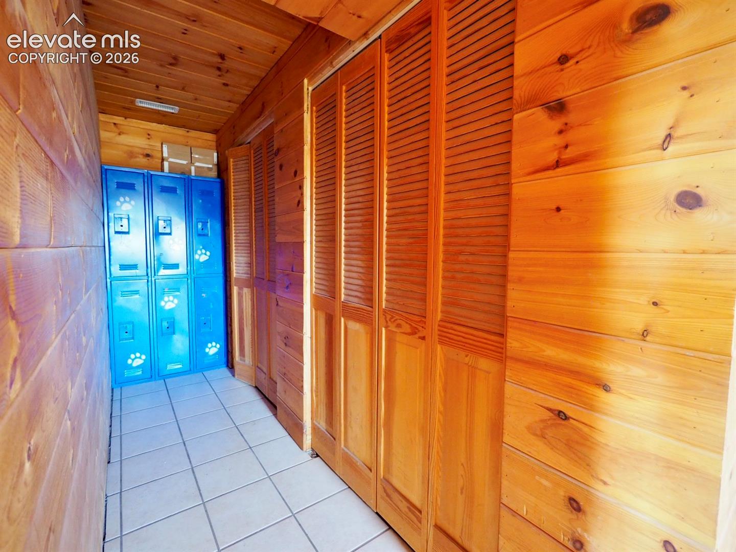Hallway featuring natural wood-paneled walls and ceiling, light-colored ceramic tile flooring, and floor-to-ceiling bifold wood closet doors