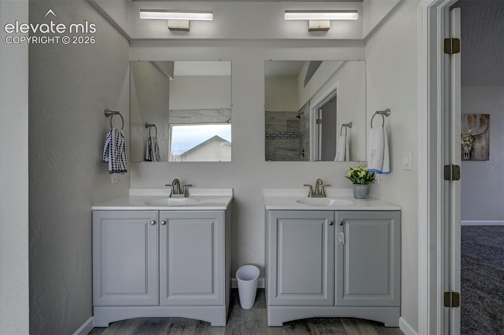 Dual vanity featuring light gray cabinetry, white countertops with integrated sinks, brushed nickel fixtures, and rectangular wall-mounted lighting