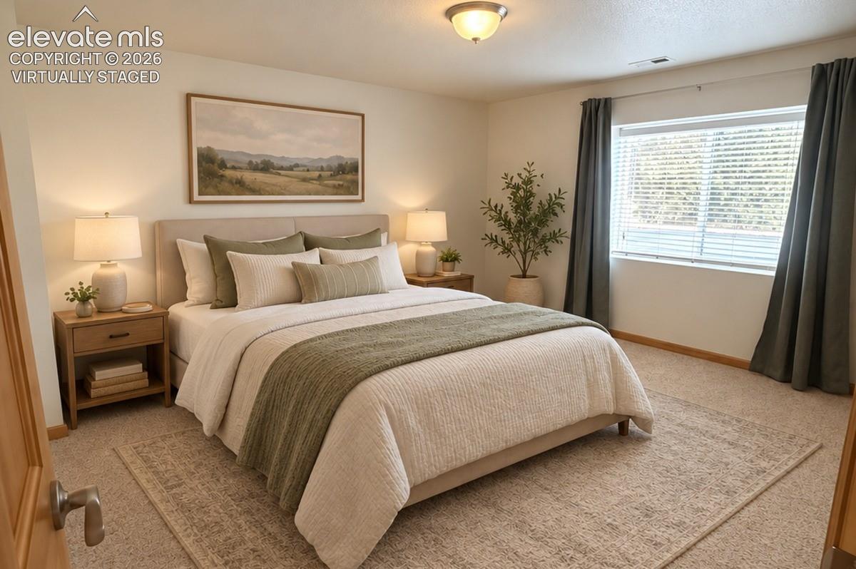 Basement bedroom 1/2. Carpeted flooring, window with blinds and drapes, ceiling-mounted light fixture, light wood-finish door. Virtually staged.