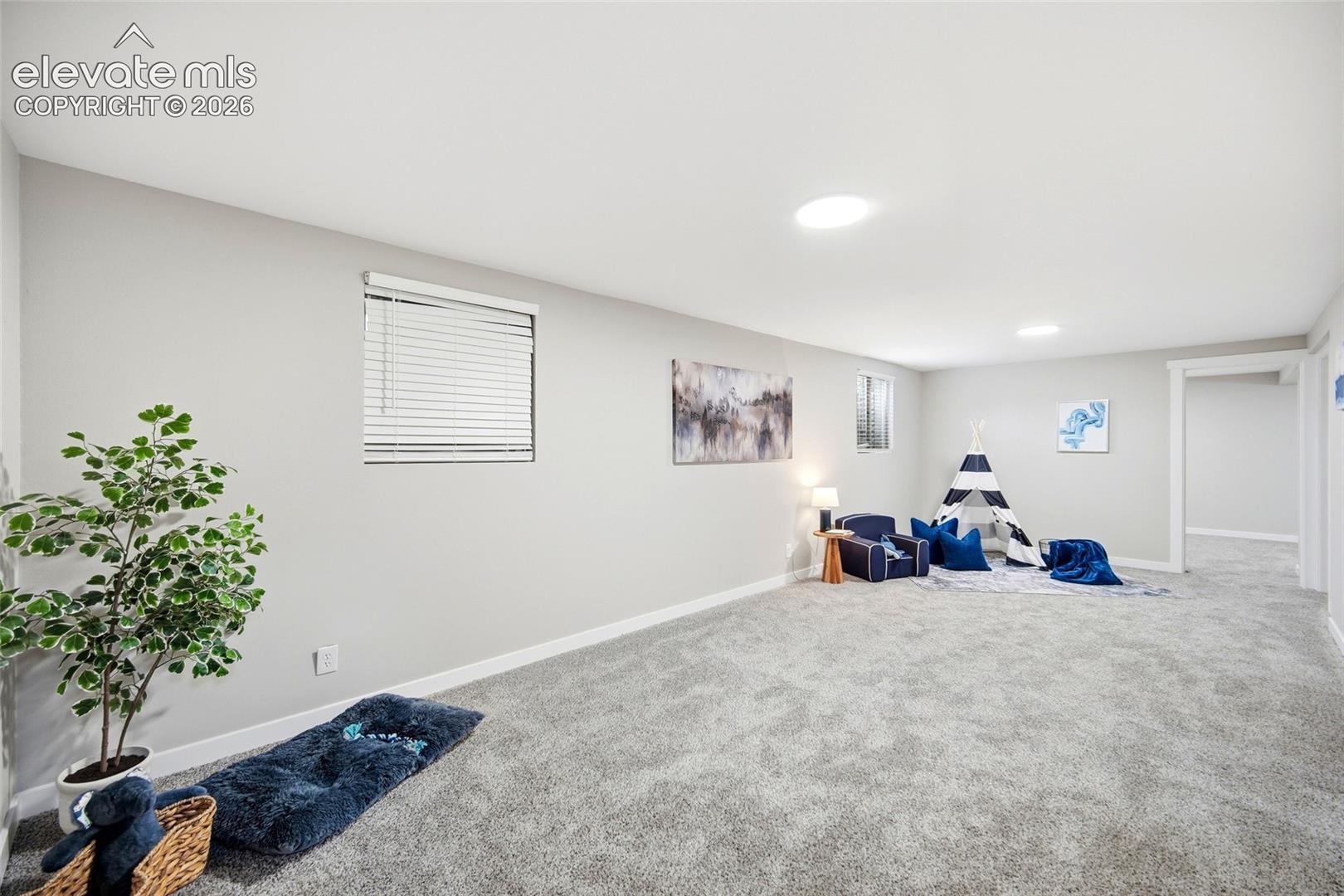 Expansive carpeted room featuring light gray walls, multiple recessed ceiling lights, and two windows with horizontal blinds