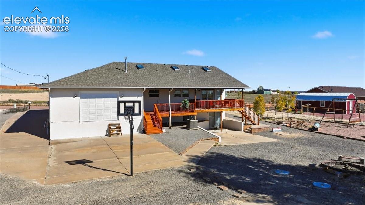 Exterior featuring a wood deck with railings, skylights, concrete patio space, and a detached structure with a pitched metal roof