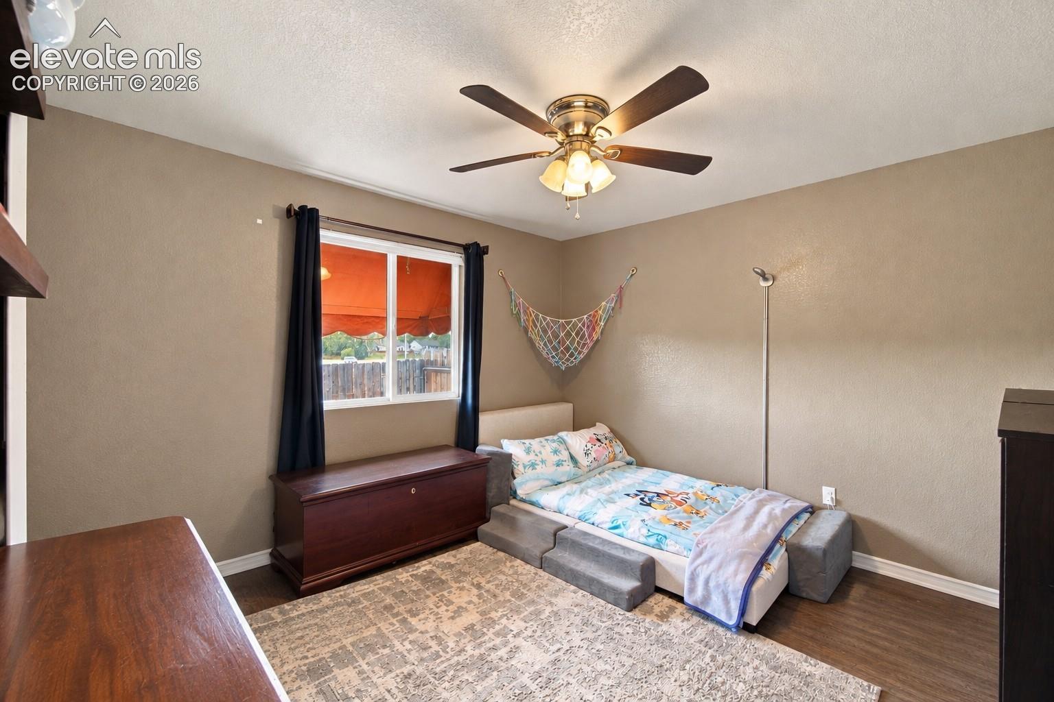 Window with dark drapery, ceiling fan with integrated lighting, wood-finish flooring, built-in shelving, and neutral wall tones