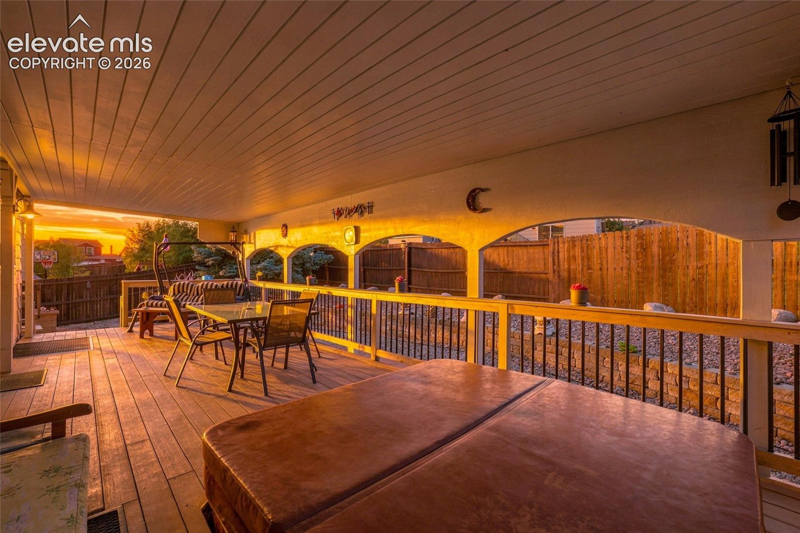 Covered wood-finish deck featuring a hot tub and arched architectural details