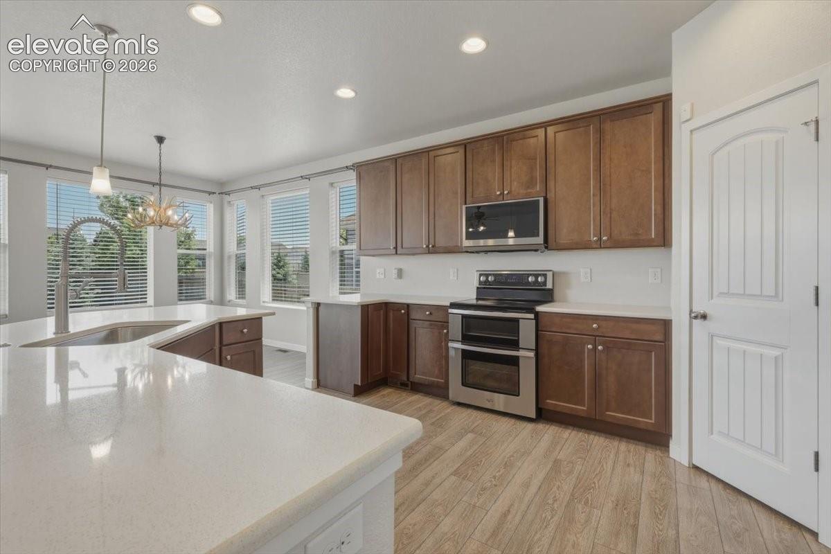 Open-concept kitchen featuring an expansive island with a stainless steel sink, light-toned countertops, wood-finish flooring, recessed lighting, and stainless steel appliances