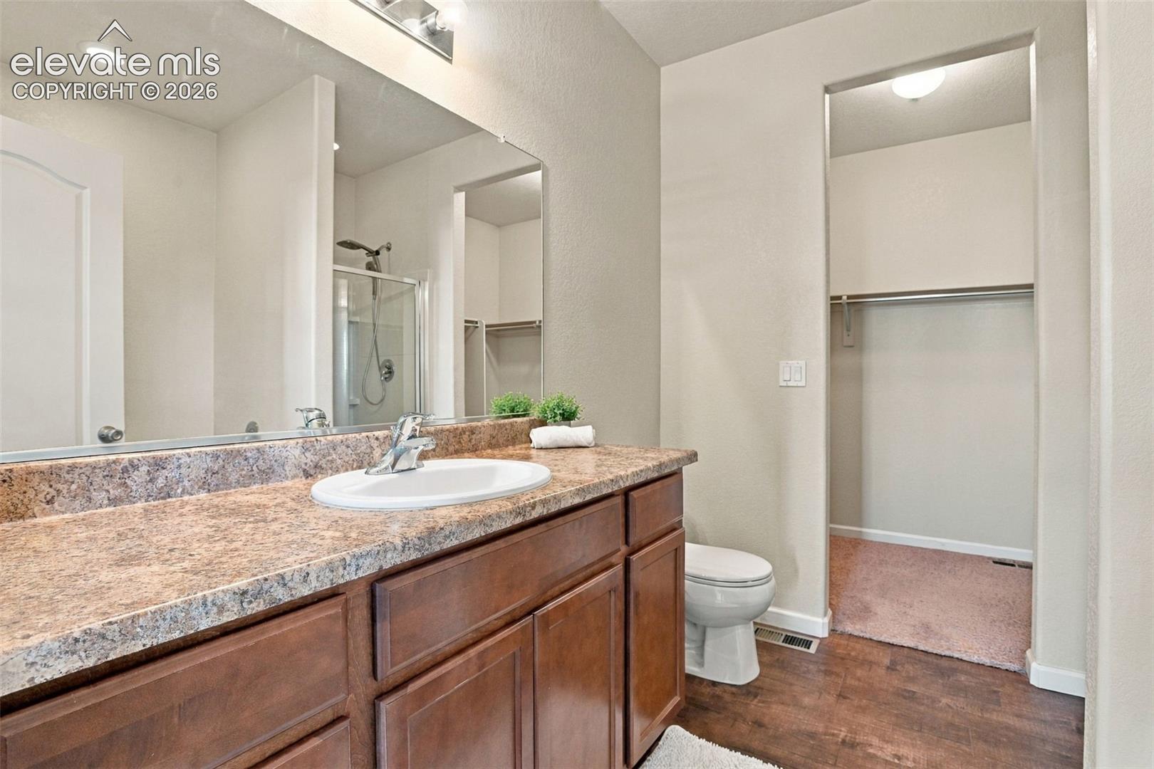 Bathroom vanity with stone-finish countertop, oval drop-in sink, wood-finish cabinetry, full-width wall mirror, and dedicated storage area
